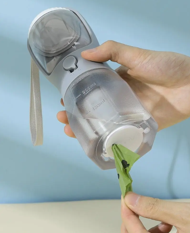 3-in-1 dog travel bottle with integrated waste-bag compartment, bag being pulled from the bottom.